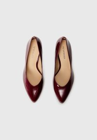 Escarpins en cuir verni bourgogne avec un bout pointu et des côtés découverts, présentant une texture lisse et une semelle intérieure beige.