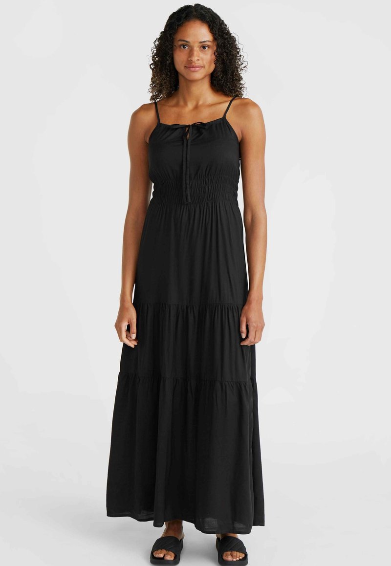 Vestido maxi negro con tirantes finos, cuerpo fruncido y falda en capas. Tejido ligero con una textura suave. Llevado con sandalias negras de tiras.