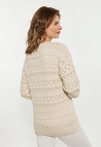 Beige gebreide trui met een gestructureerd patroon met opengewerkte ruitvormen. Ribbelkraag en boorden, lange mouwen en een relaxte pasvorm.