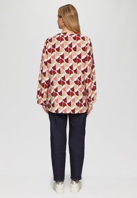 Langsleeve shirt met een geometrisch patroon in rode, beige en roze tinten. Gepaard met donkerdenim broek en metallic sneakers.