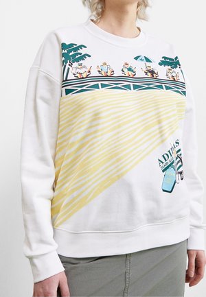 Bílá mikina s grafikou lidí odpočívajících na dřevěné promenádě, palem, žlutého písku a sandálů s nápisem "ADIDAS Island Club".