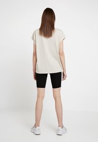 Vaalean beige lyhythihainen t-paita, jossa on rento istuvuus, yhdistettynä mustiin pyöräilyshortseihin ja valkoisiin urheilukenkään. Yksinkertainen muotoilu, sileä kangas.