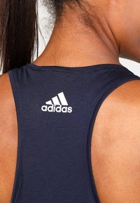 Camiseta sin mangas deportiva en color navy, fabricada con tejido suave, con un cuello redondo y el logo blanco de Adidas en la parte posterior, cerca del hombro.