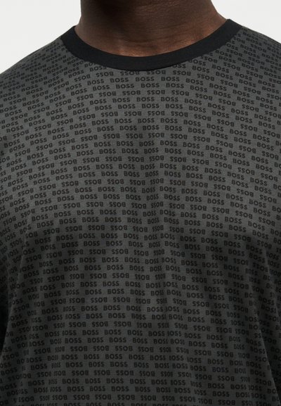 Chemise gris foncé avec col rond noir, couverte de petits textes "BOSS" répétés sur tout le tissu.