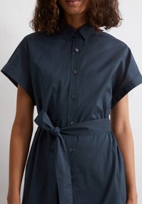 Abito camicia blu navy con colletto, maniche corte, chiusura a bottoni e cintura legata in vita, realizzato in un tessuto morbido.