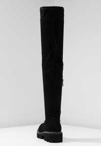 Bottes noires montantes au-dessus du genou en daim souple, dotées d'une semelle épaisse, d'une fermeture éclair latérale et d'une texture lisse sans motifs visibles.