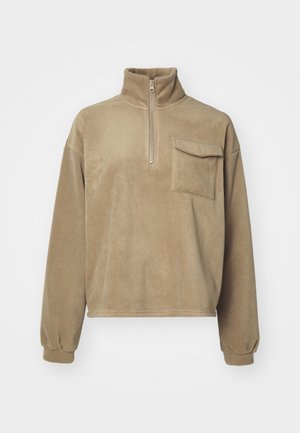 Bež flis pulover z visokim ovratnikom, 1/4 zadrgo in žepom na prsih. Ima ohlapne rokave z elastičnimi manšetami in mehak teksturo.