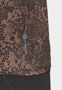 Camiseta atlética marrón con un patrón de estampado animal negro y un pequeño logo azul "AEROREADY". Textura suave con un diseño ajustado.