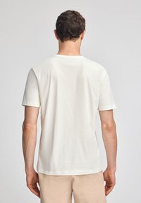 T-shirt in cotone crema con scollatura a girocollo e maniche corte, caratterizzata da una texture liscia e un design a taglio dritto sul retro.