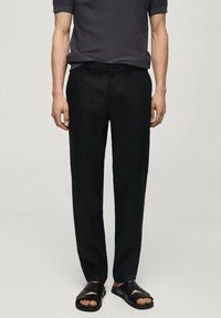 I pantaloni neri in lino hanno un design a gamba dritta e una chiusura con bottone. Il tessuto ha una consistenza liscia, abbinato a sandali neri casual.