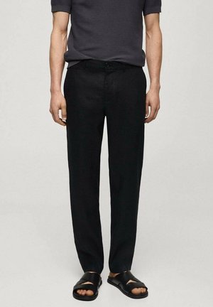 I pantaloni neri in lino hanno un design a gamba dritta e una chiusura con bottone. Il tessuto ha una consistenza liscia, abbinato a sandali neri casual.