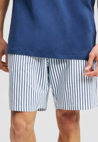 T-shirt in cotone blu navy abbinato a pantaloni corti bianchi con sottili righe verticali blu navy, rifiniti con orli semplici e una vestibilità rilassata.