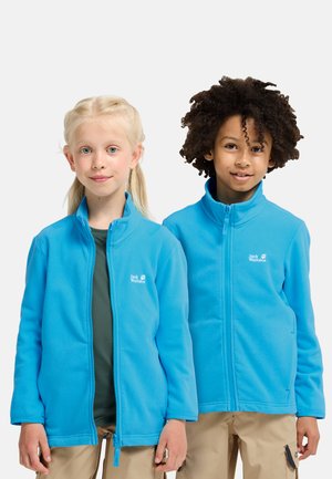 Twee kinderen dragen felblauwe Jack Wolfskin fleecejacks en staan naast elkaar tegen een effen witte achtergrond.
