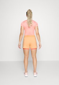 Vaaleanpunainen lyhythihainen paita yhdistetty oransseihin shortseihin. Shortseissa on sileä pinta ja tiukka malli, jotka on yhdistetty vaaleanpunaisiin urheilukenkiin.