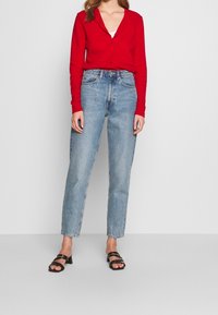 Rot cardigan mit langen Ärmeln und Knopfleiste, kombiniert mit hoch taillierten hellblauen geraden Jeans und schwarzen Riemchen-Heels.