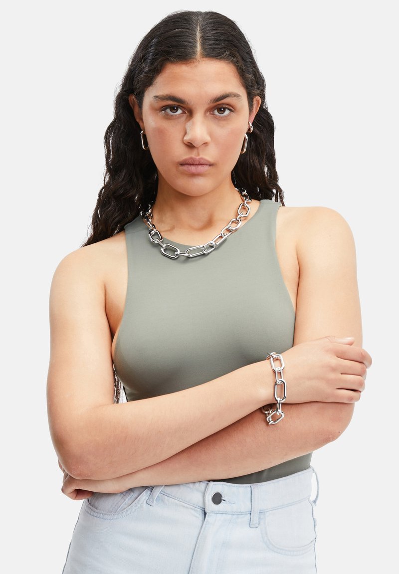Olijfgroene mouwloze top, zilveren ketting en armband, lichte denim jeans, met een zachte textuur en een aansluitend ontwerp.