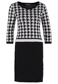 Robe en maille présentant un motif pied-de-poule noir et blanc sur le haut, tissu noir uni en dessous, avec un col rond et des manches trois-quarts.