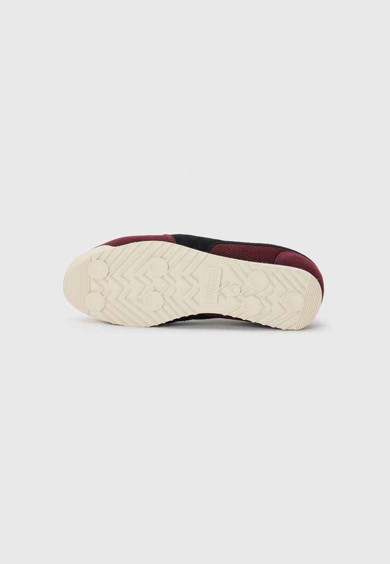 Zwarte en bordeauxrode sneaker met een gestructureerde bovenzijde, voorzien van een dikke, witte rubberen zool met een zigzagprofiel.