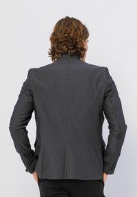 Donkergrijze blazer met een gladde textuur, getailleerde pasvorm en subtiele stikseldetails. Heeft een hoge kraag en manchetten met drie knopen.