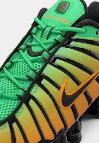 Topánky Nike Shox s priedušným zvrškom v zelenej farbe prechádzajúcej do oranžovej, so čiernymi akcentmi, výraznými šnúrkami a technológiou odpruženia Shox.