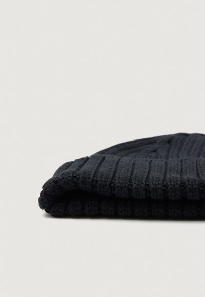 Donker marineblauwe gebreide beanie muts plat gevouwen op een effen lichte achtergrond.