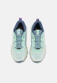 Scarpe da corsa azzurro chiaro con tomaia texture, caratterizzate da un'etichetta Gore-Tex, accenti viola e una suola ammortizzata per il comfort.