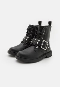 Botas de tobillo de cuero negro con puntera redonda, cierre de cordones en la parte delantera y una correa con tachuelas que presenta una hebilla de plata en el empeine. Superficie texturizada.