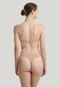 Ensemble de sous-vêtements rose sans couture avec des bretelles réglables et un dos à fermoir. Il présente une texture lisse et un design minimaliste.