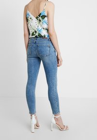 Vaqueros pitillo azules combinados con una camiseta de tirantes con estampado floral, con tirantes finos y espalda en forma de V. Modelo con sandalias blancas de tacón.