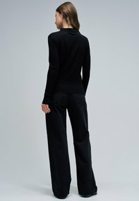 Suéter negro de manga larga con un diseño ajustado y textura acanalada, combinado con pantalones anchos negros. Vista desde la parte posterior.