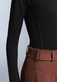 Black long-sleeve top with textured fabric, paired with brown high-waisted pants featuring a ribbed belt and zipper pocket details.
