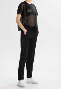 Top corto a maniche corte in rete nera, abbinato a pantaloni neri a sigaretta con strisce laterali in satin e scarpe da ginnastica bianche.