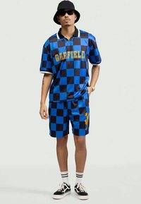 Camisa polo xadrez azul com o texto dourado "GARFIELD", combinada com calções com um padrão semelhante e um detalhe gráfico amarelo.