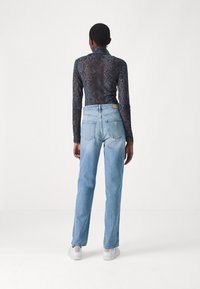 Camiseta de manga larga con un diseño de estampado de serpiente oscuro, combinada con jeans rectos de color azul claro y zapatillas blancas. Líneas limpias y texturas distintas.