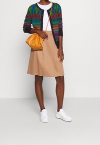 Farverig strikket cardigan med geometriske mønstre, hvid t-shirt, beige nederdel og gul håndtaske. Afsluttet med hvide sneakers.