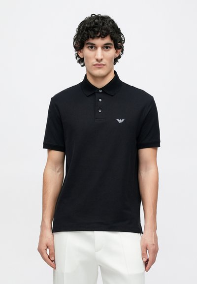 Čierne bavlnené polokošeľa s golierom a trojradovým zapínaním na gombíky. Vyšívané logo na ľavej strane hrudníka. Krátke rukávy.