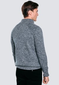 Szary sweter dzianinowy z wysokim kołnierzem, textured tkaniną i prążkowanymi mankietami. Cechuje się luźnym krojem i noszony jest na czarnych spodniach.