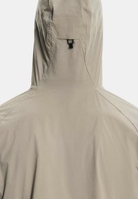 Bēšas krāsas kapuce ar teksturētu virsmu, kas aprīkota ar auklu ap kaklu un aizmugurē ir kabata uzglabāšanai.