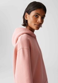Felpa rosa in cotone con un ampio cappuccio, spalle abbassate e una finitura texturizzata. Design semplice senza motivi o accenti visibili.