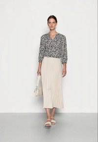 Blusa com padrão floral e decote em V, combinada com uma saia midi plissada bege. Os acessórios incluem uma pequena mala e sandálias leves.