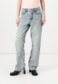 Lyse blå rette jeans med slitt vask, fem-lommers design, beltehemper og kontraststing. Brukt med svarte høye sko.