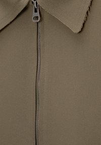 Veste kaki avec un détail de fermeture éclair à l'avant, un col et une texture de tissu lisse avec une finition soignée le long des bords.