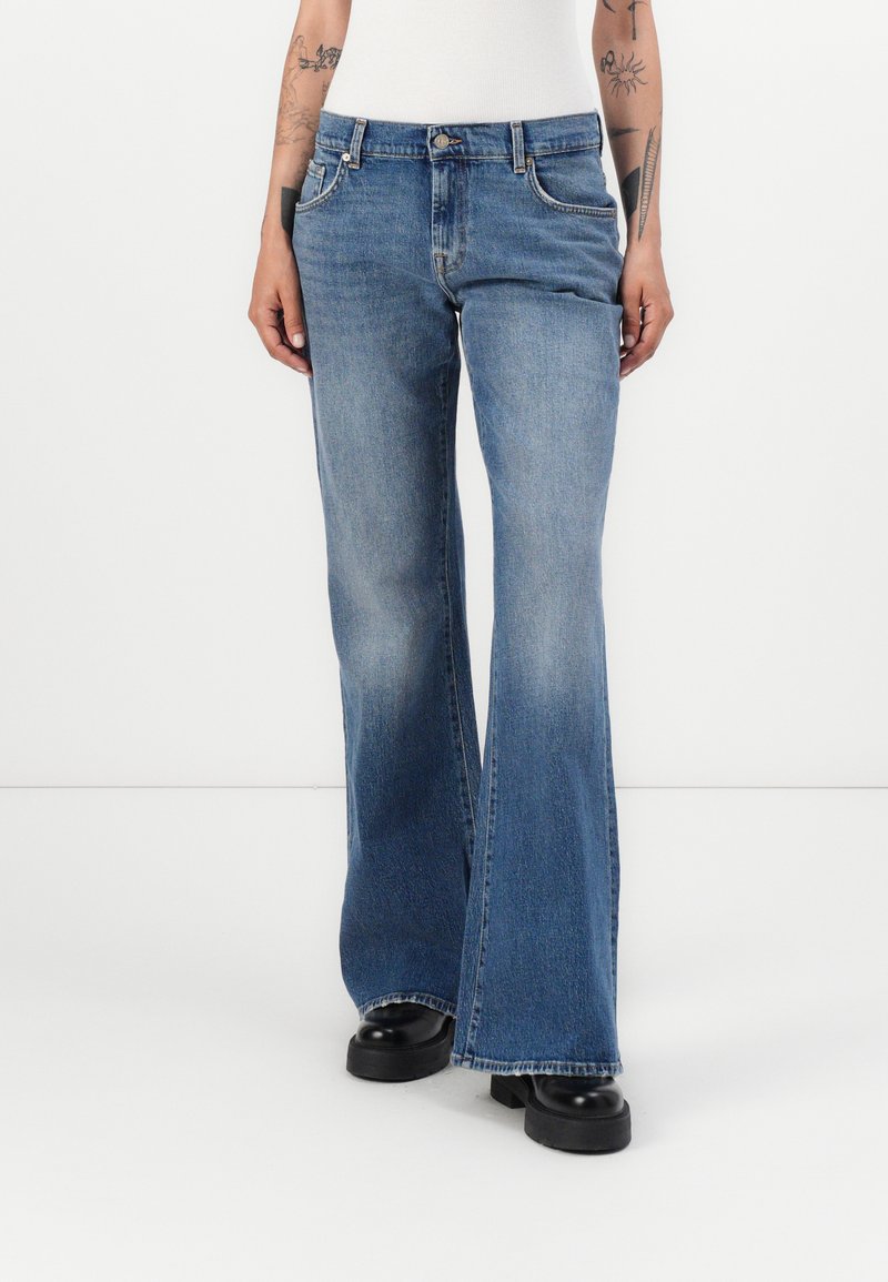 Light blue flared jeans made of denim, featuring a five-pocket design, mid-rise waist, and subtle fading with white stitching accents.
