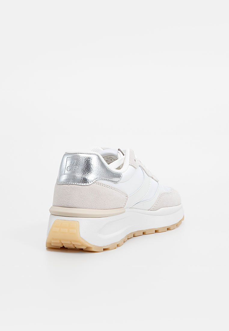 Sneaker blanc et beige avec détail de talon en argent, semelle texturée et design à lacets, vue du côté arrière droit sur fond blanc.