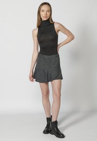 Mustat hihattomat bodysuitit yhdistettynä ruudulliseen mini-hameeseen, jossa on valuma-asymmetrinen muotoilu. Mustat nauhalliset sotilaskengät viimeistelevät asun.