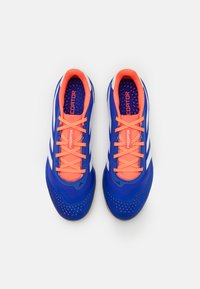 Zapatos de fútbol azules con un upper texturizado, cordones naranjas y rayas blancas. Incluyen una suela de goma con perforaciones para transpirabilidad.