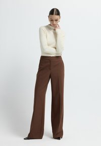 Crème ribbel turtlenecktrui gecombineerd met hoge taille, wijde bruine broek. Slanke silhouette met minimale details en een gladde textuur.