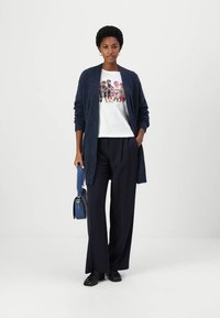 Cardigan bleumarin cu deschidere în față, tricou alb cu un grafic colorat de animal, pantaloni largi bleumarin și o geantă de umăr albastră.