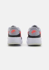 Baskets de sport grises avec un design noir et rouge. Tige en maille texturée, col rembourré et semelle en caoutchouc blanche. Détail du logo à l'arrière visible.