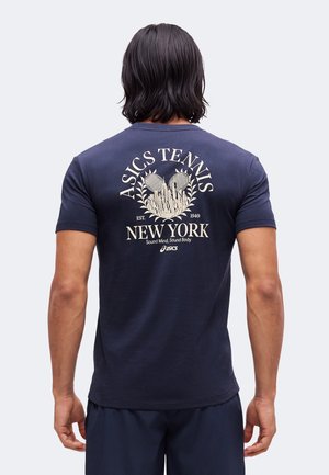 Homme aux cheveux noirs mi-longs portant un t-shirt bleu marine Asics Tennis New York avec un graphisme et du texte au dos.
